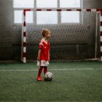 Child Playing Indoor Football In Red Kit